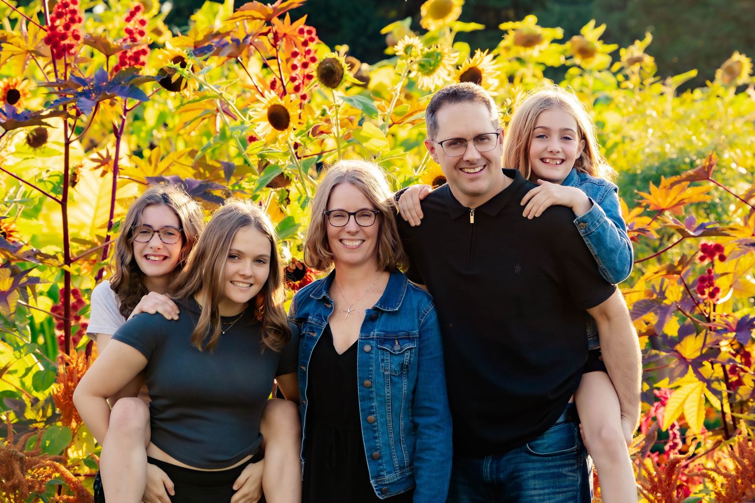 People gathered in front of autumn foliage wearing casual attire and denim in warm evening light.
