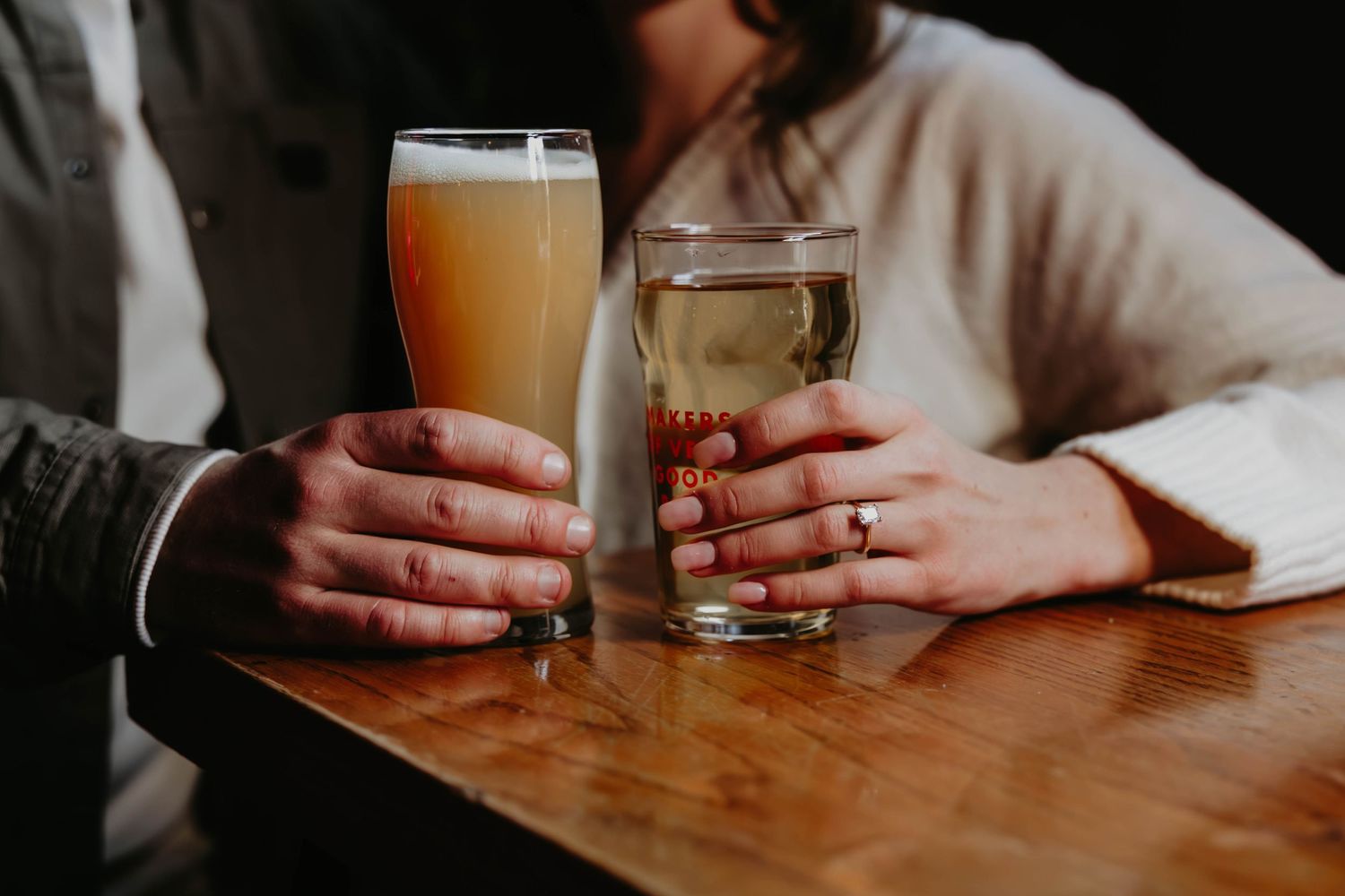 Hands holding coffee mugs on a wooden table in dim lighting.