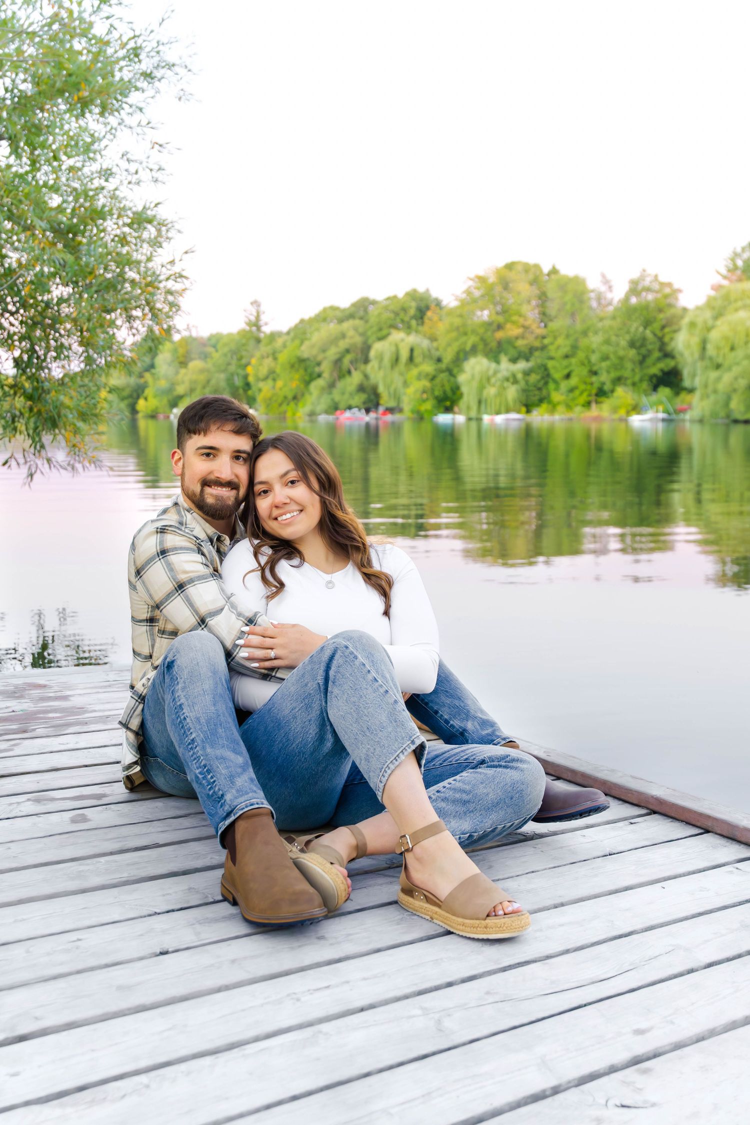 Couple relaxing together on wooden dock by serene lake during sunset photoshoot.