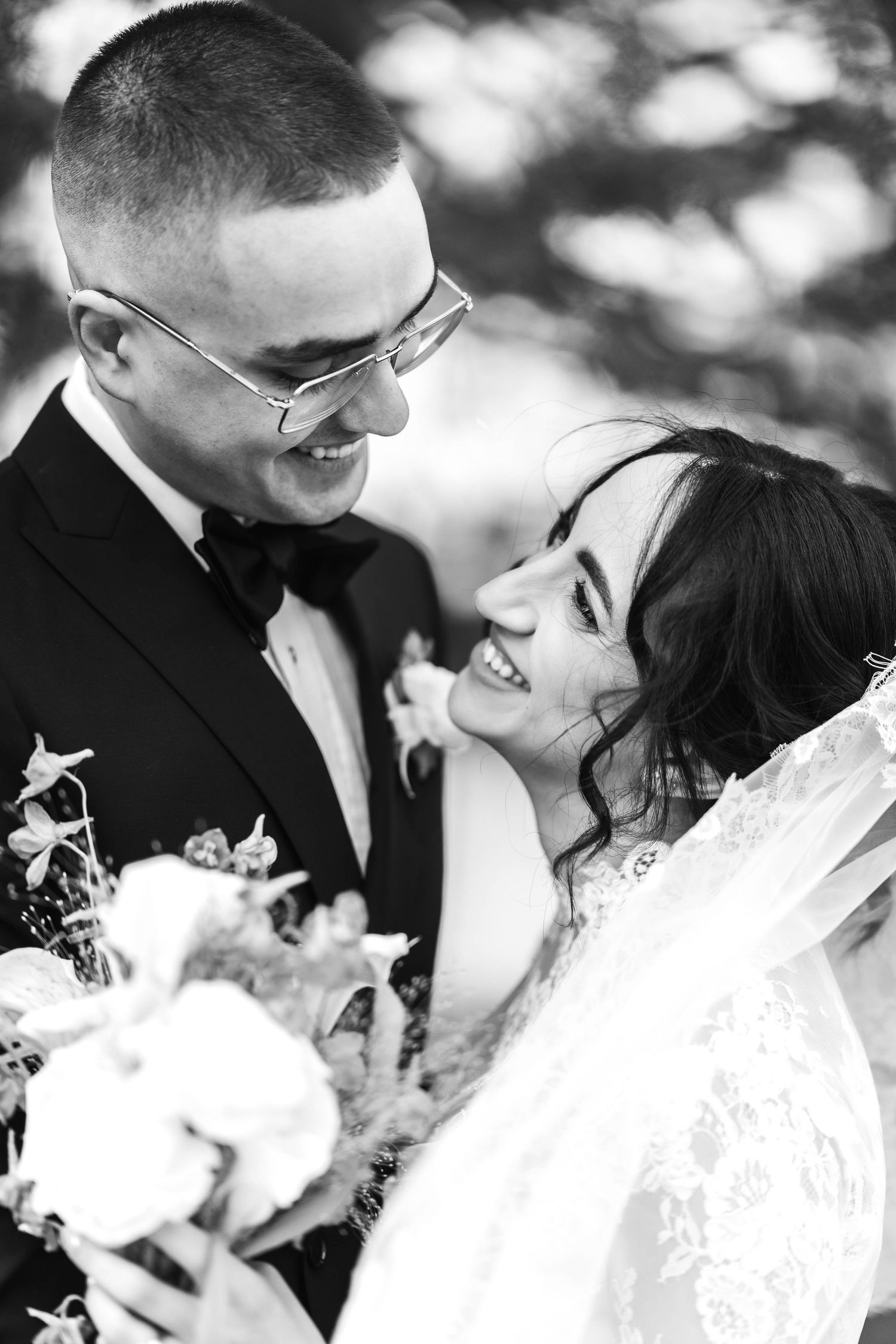 Black and white photo of smiling bride and groom sharing a joyful moment outdoors on their wedding day.