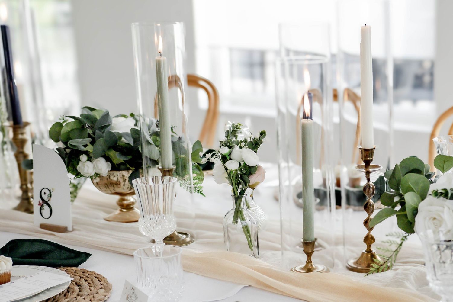 Light-filled wedding reception table with brass details and eucalyptus greenery.