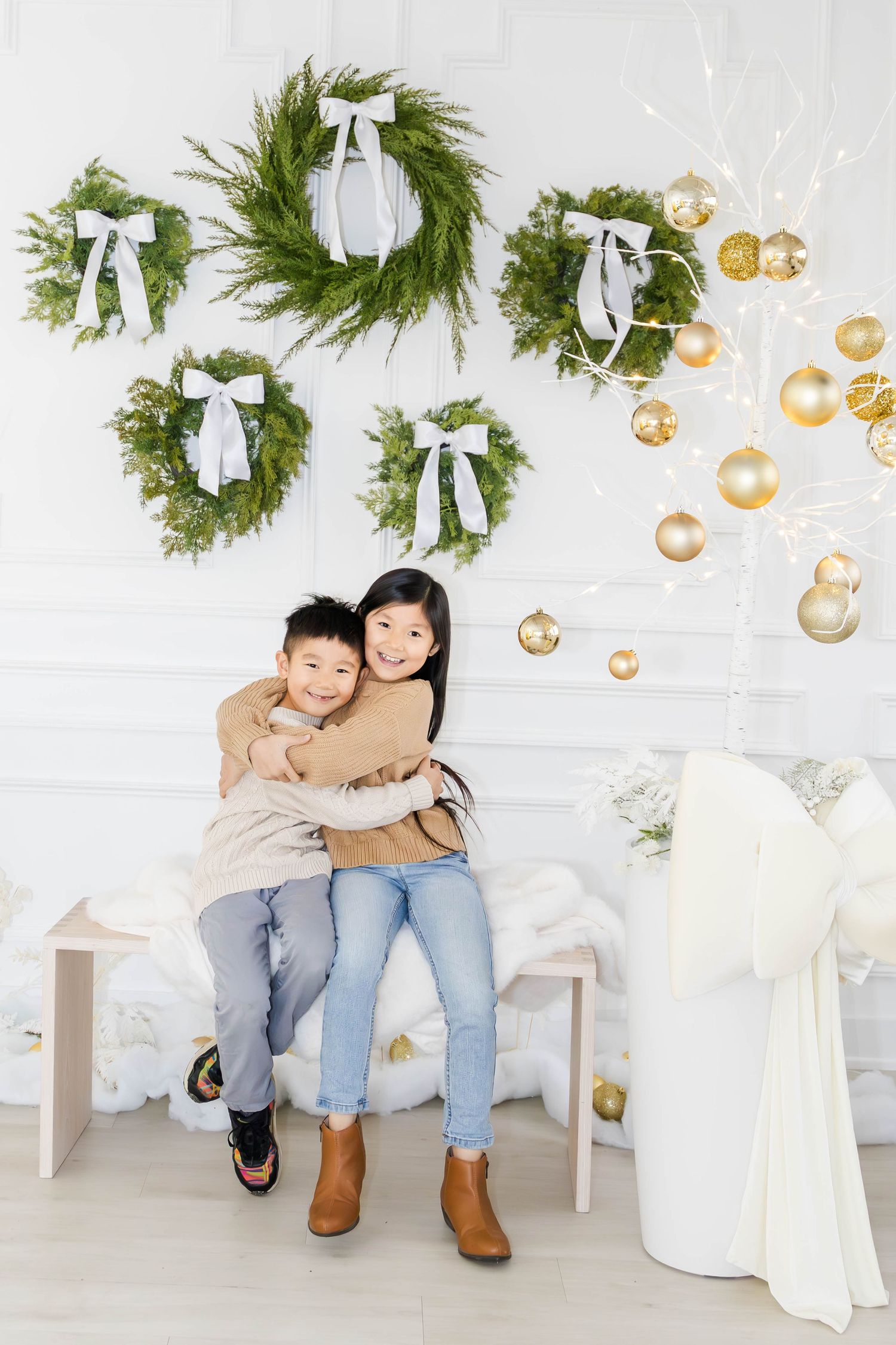 Family holiday photos with gold ornaments and evergreen wreaths on white wall.
