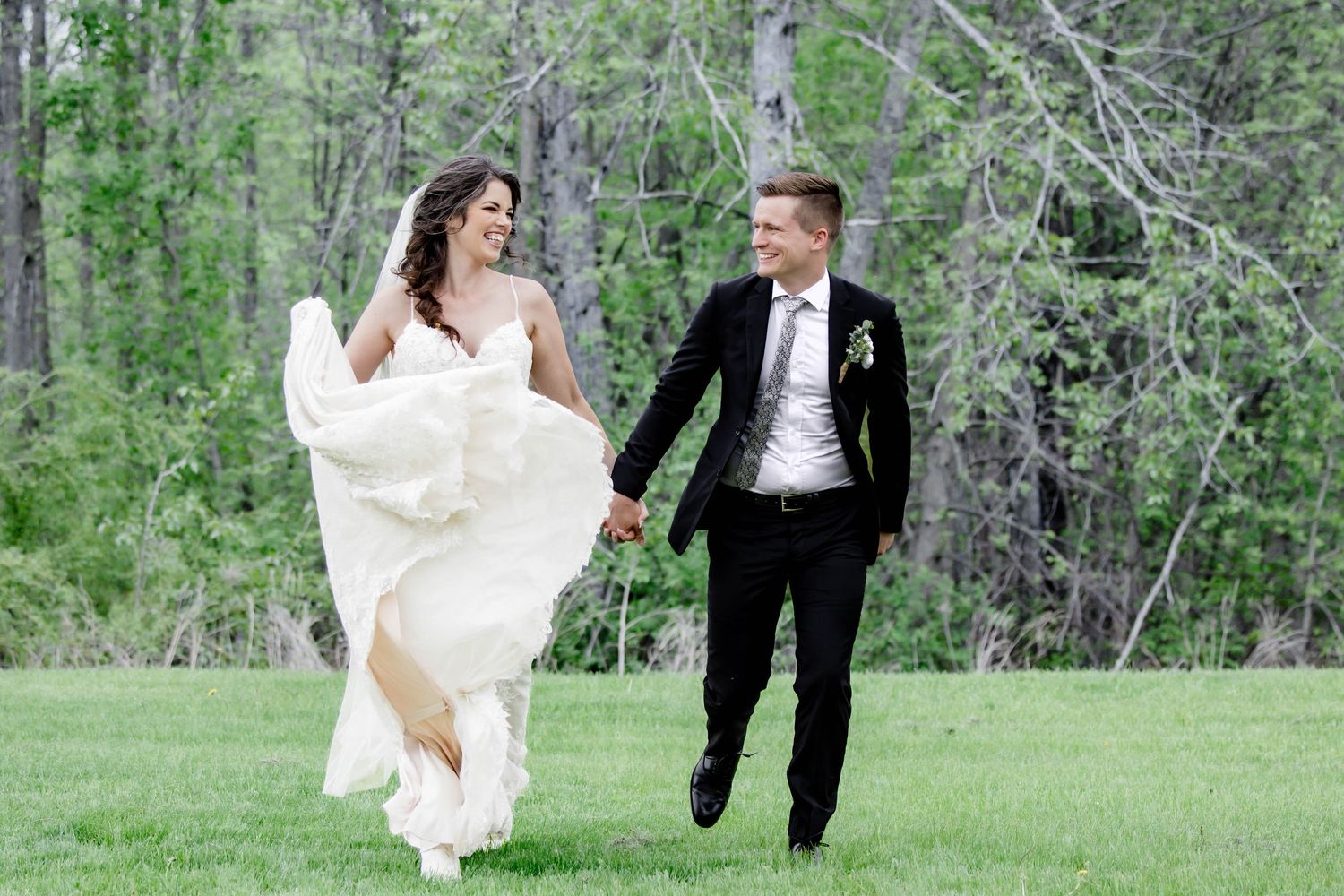 A couple in wedding attire walks together through a lush green forest setting during a photo session.