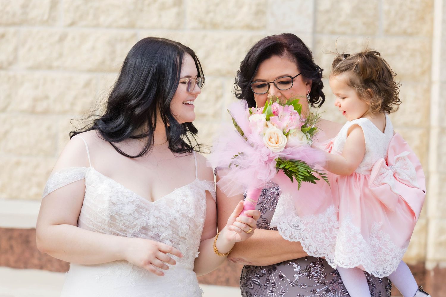 Wedding party sharing joyful moments outside a stone building with pink floral accents.