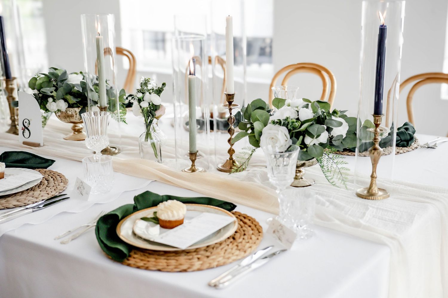 Minimalist wedding tablescape featuring woven chargers, brass candlesticks, and white table linens.