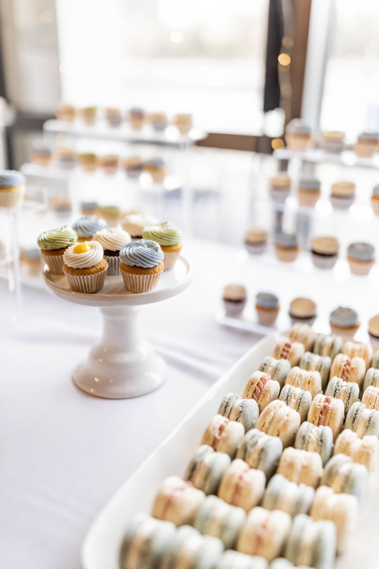 Elegant wedding dessert table with pastel cupcakes on a white cake stand and rows of macarons.