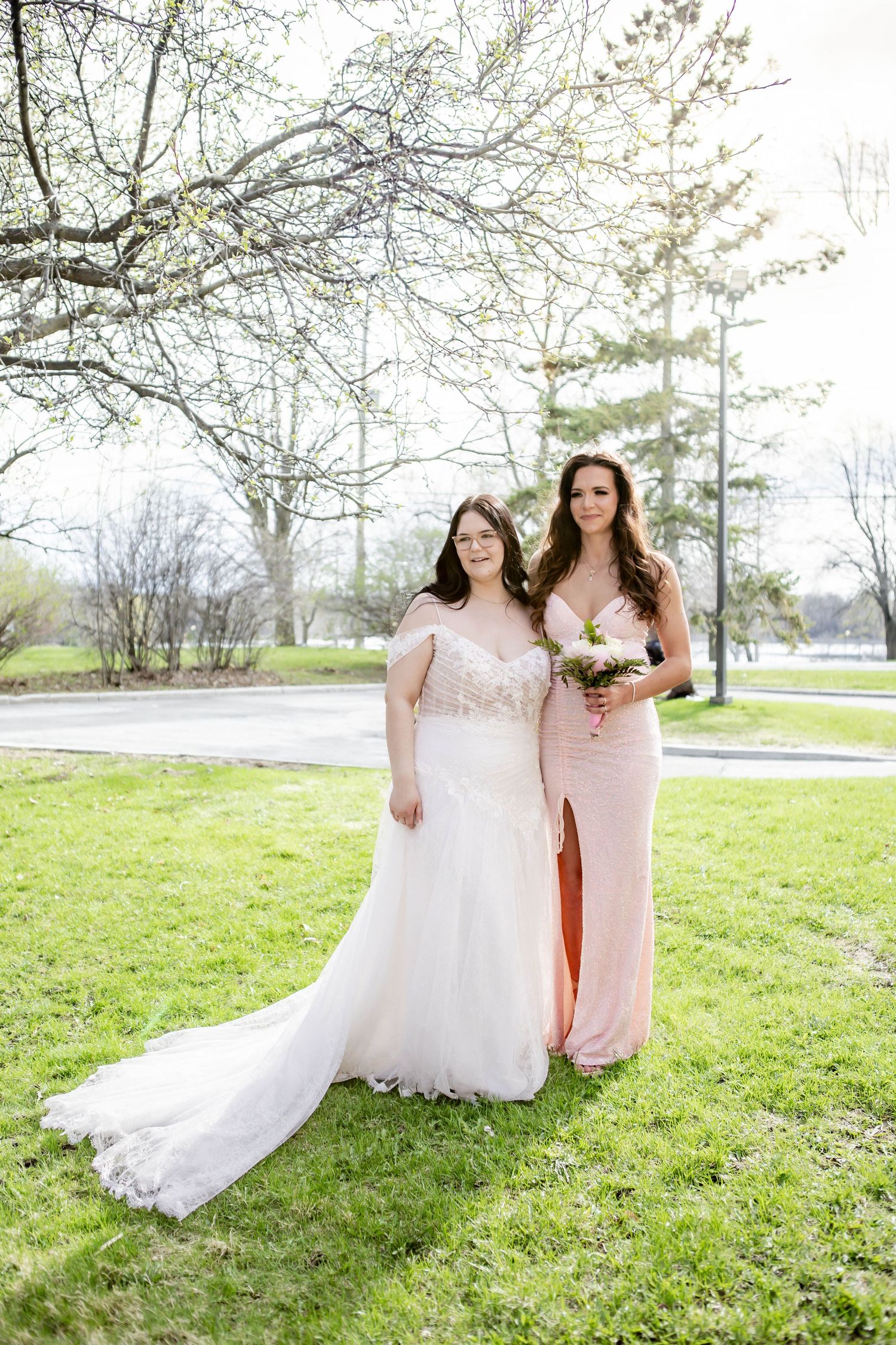 Wedding group poses on spring lawn with flowing white gown and pink bridesmaid dresses.
