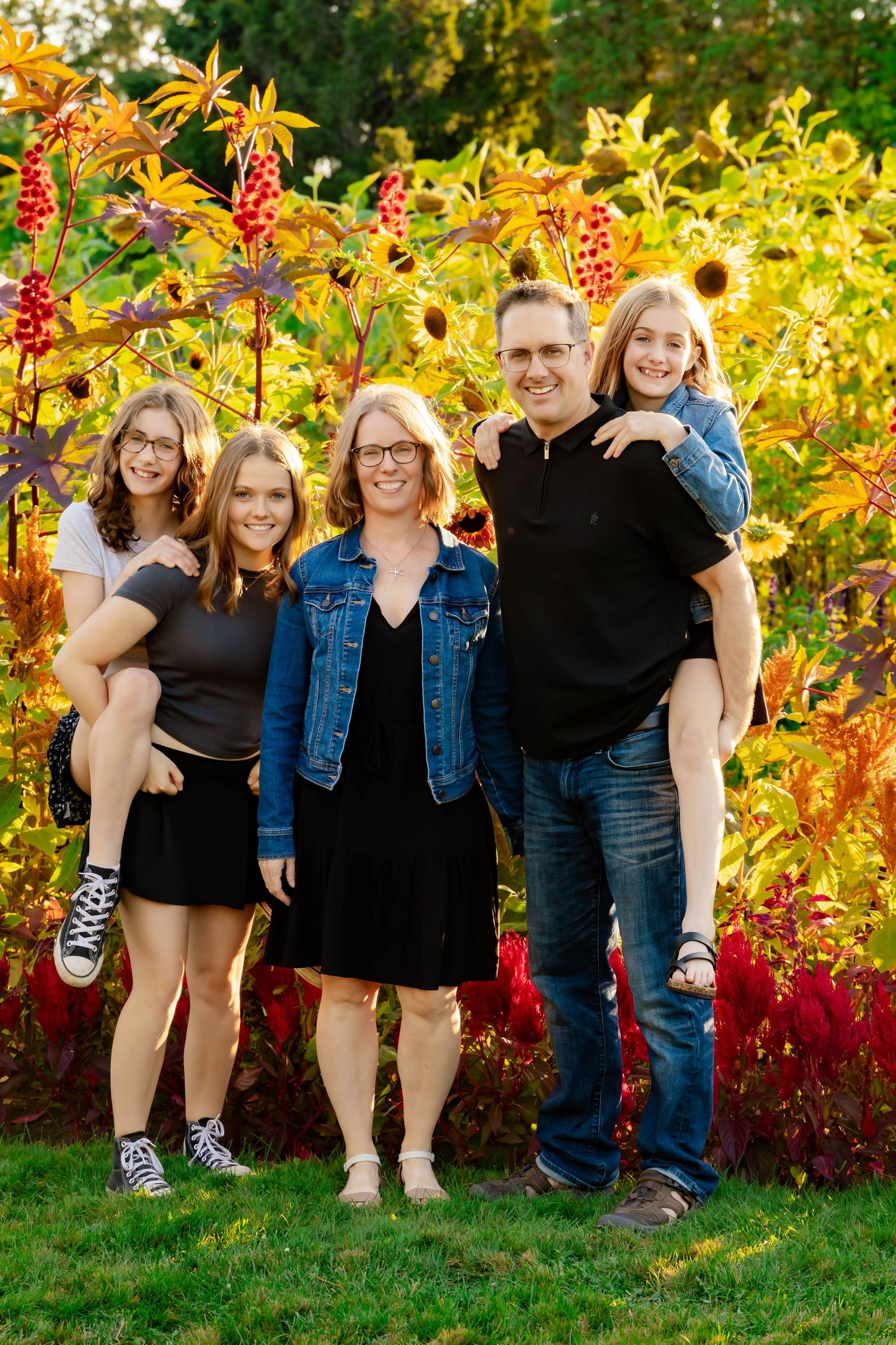 A group poses together against vibrant fall foliage with red and yellow leaves in an outdoor garden setting.