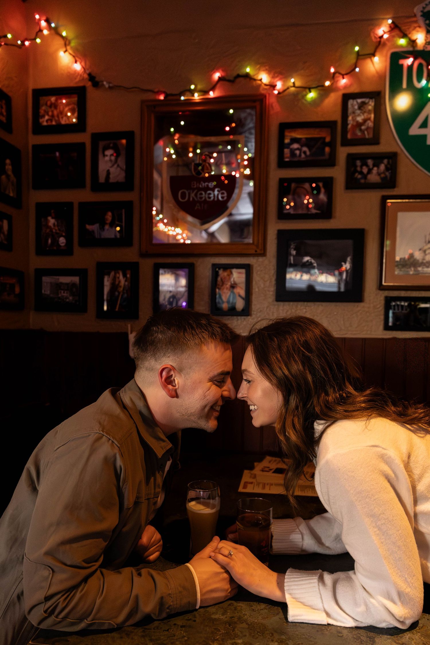 Romantic couple sharing intimate moments under warm string lights in a cozy room decorated with framed photos.
