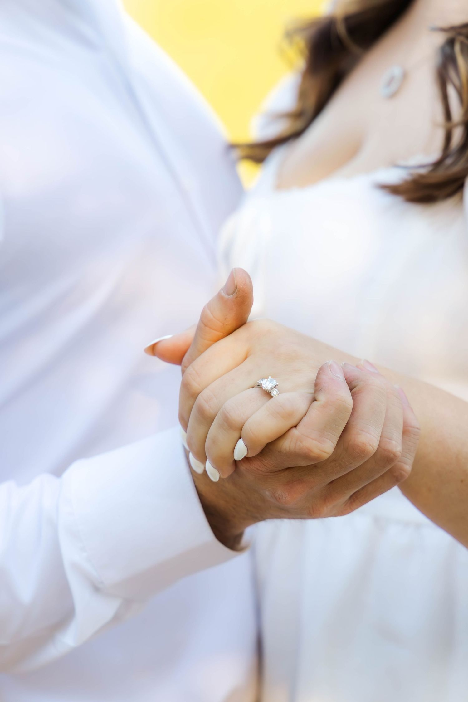Close-up view of hands wearing a white long sleeve shirt against a bright yellow background.