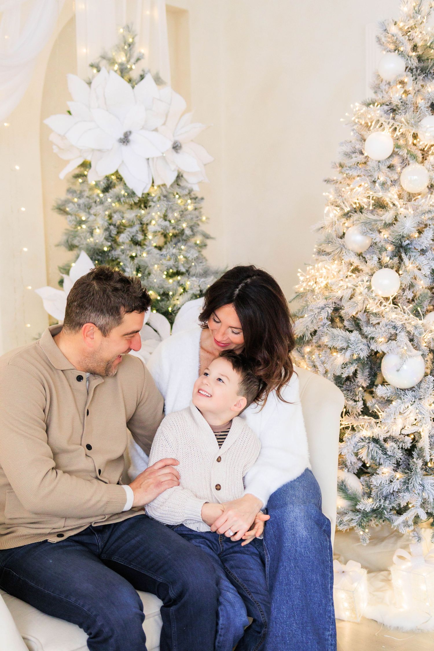 An intimate family portrait in front of illuminated Christmas trees decorated with white flowers and ornaments.