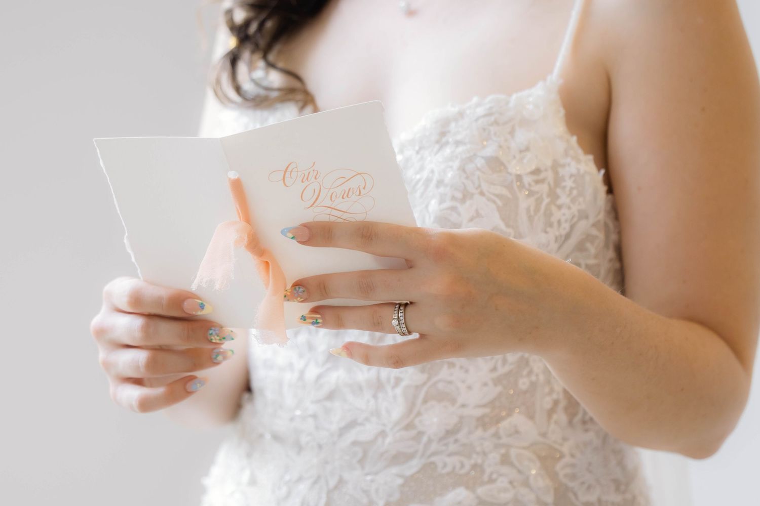 Close up view of hands holding a handwritten note while wearing an elegant white lace wedding dress.