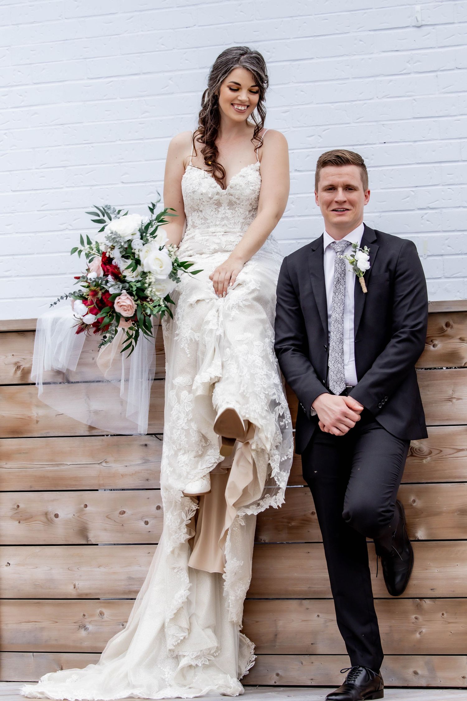 Modern wedding portraits against white brick wall with rustic wooden accents.