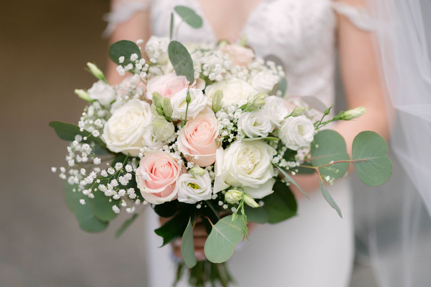 Bride holding a romantic wedding bouquet with blush pink roses, white lisianthus, baby's breath, and eucalyptus greenery.
