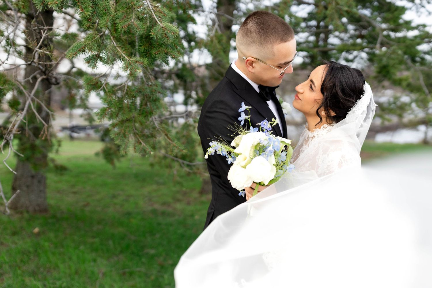 Bride and groom share a romantic moment outdoors, with her flowing white gown and bouquet of white flowers.