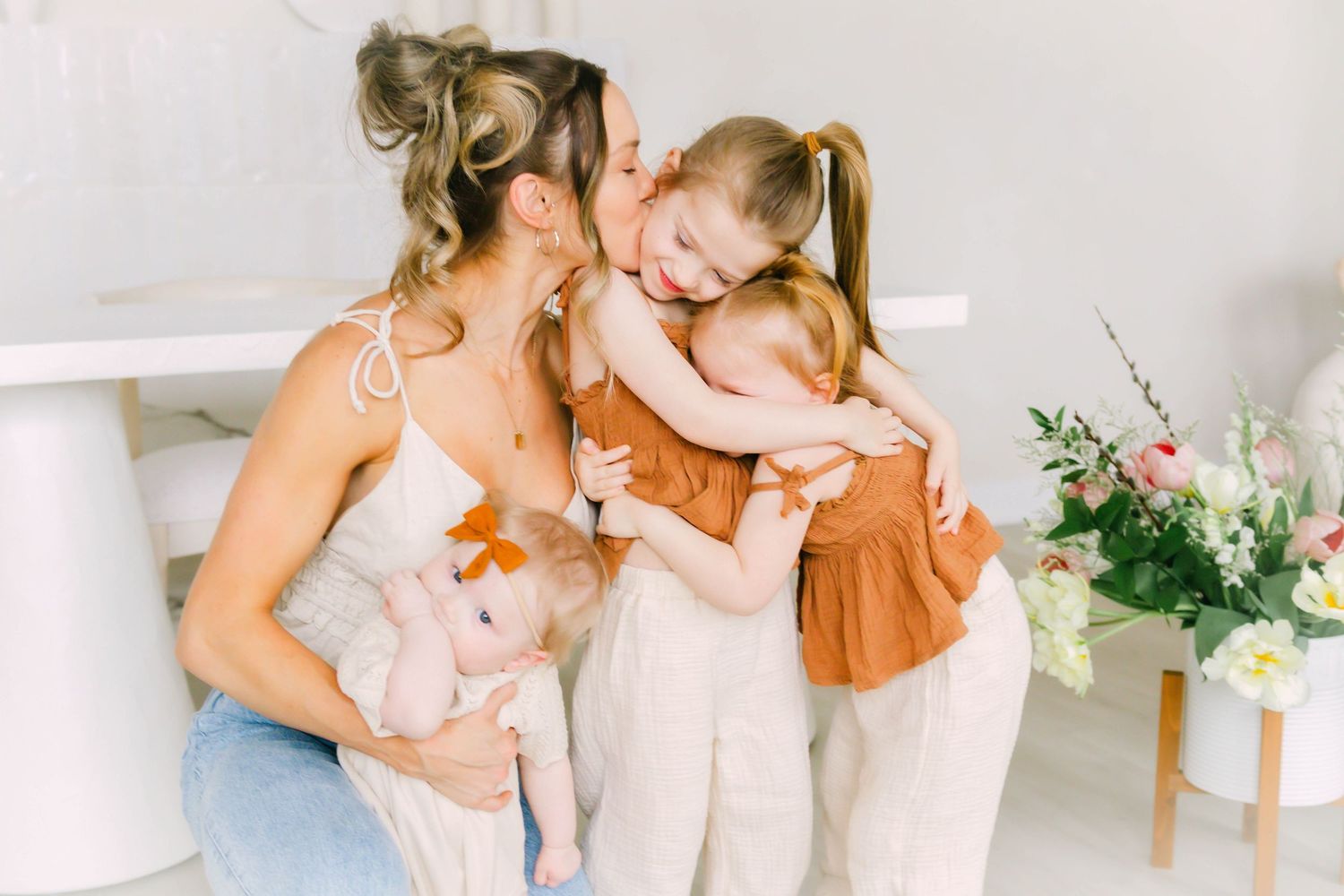 A tender family moment shared on a white couch with soft lighting and floral decor in the background.