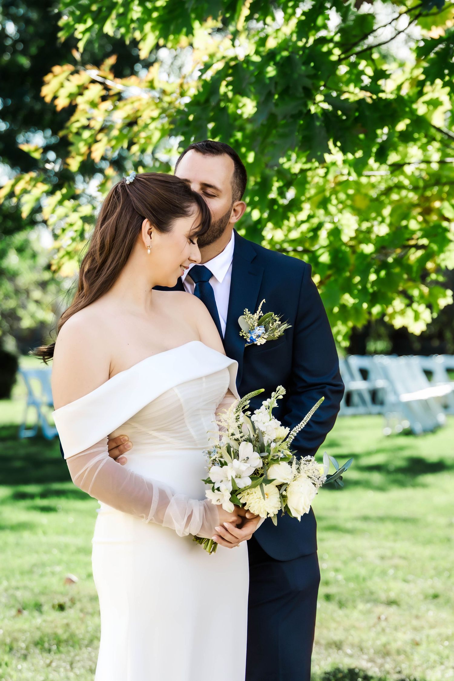 Newlyweds share intimate moments in a sunlit garden with white flowers and elegant attire.