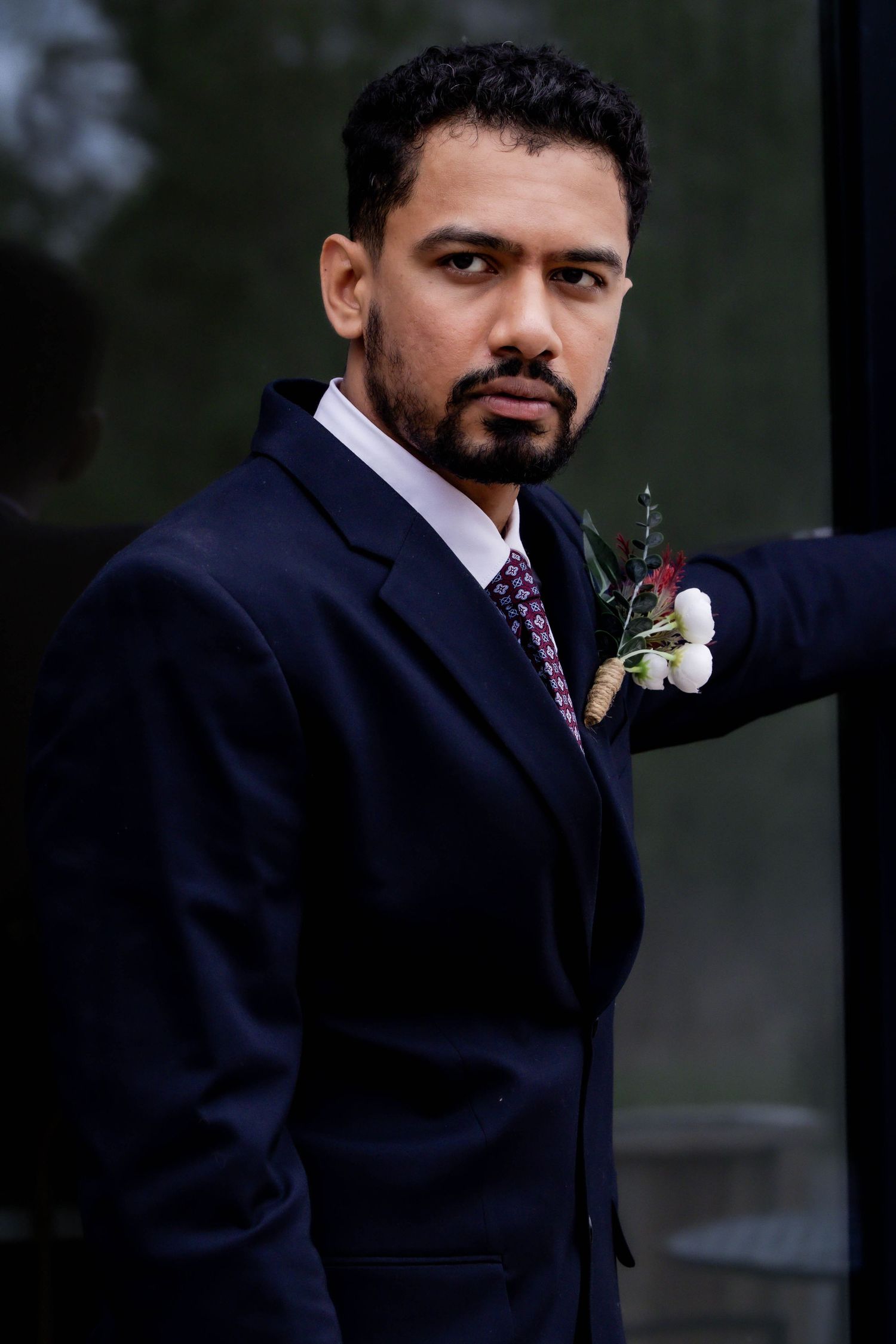 A groom in a navy suit with a boutonniere poses during a formal wedding photoshoot.