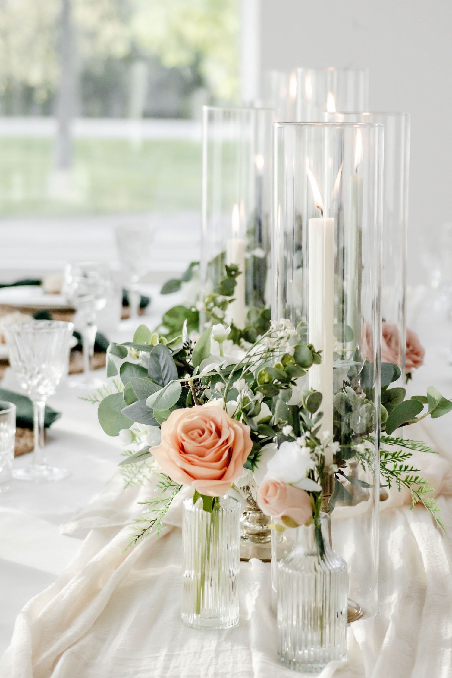 Elegant wedding table centerpieces with peach roses, eucalyptus, and tall glass candle holders.