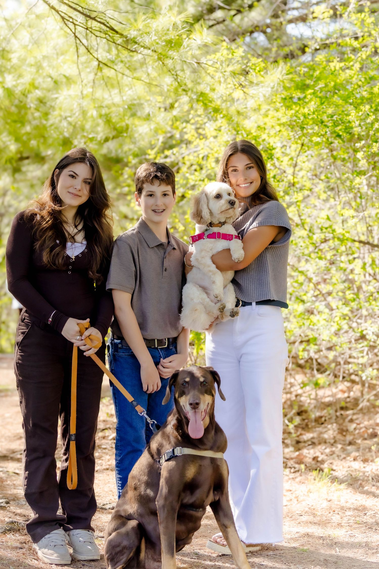 Family members and their pets gather for casual portraits in a sunlit outdoor setting.