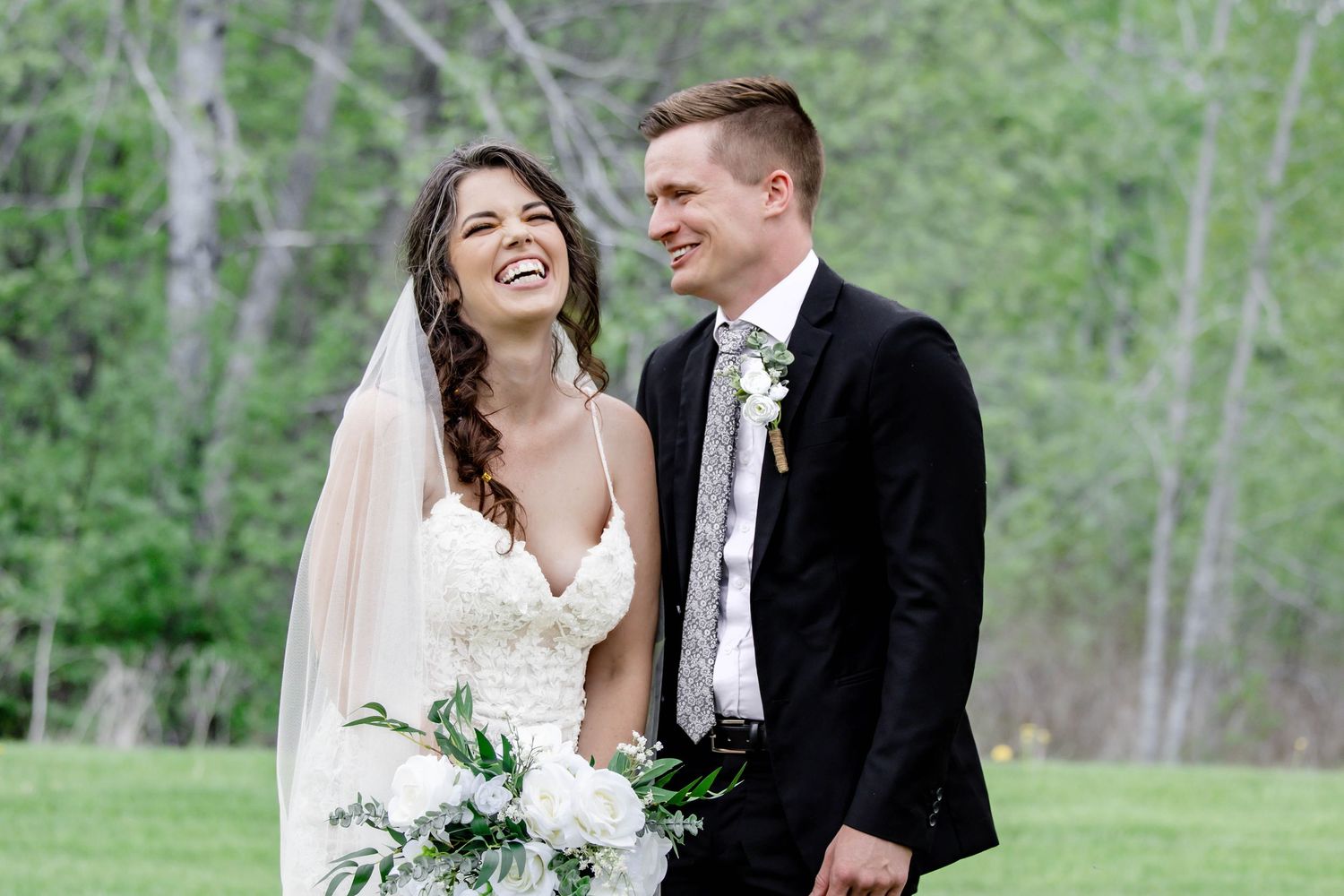 A romantic wedding couple shares a tender moment together in a natural outdoor setting with trees in the background.