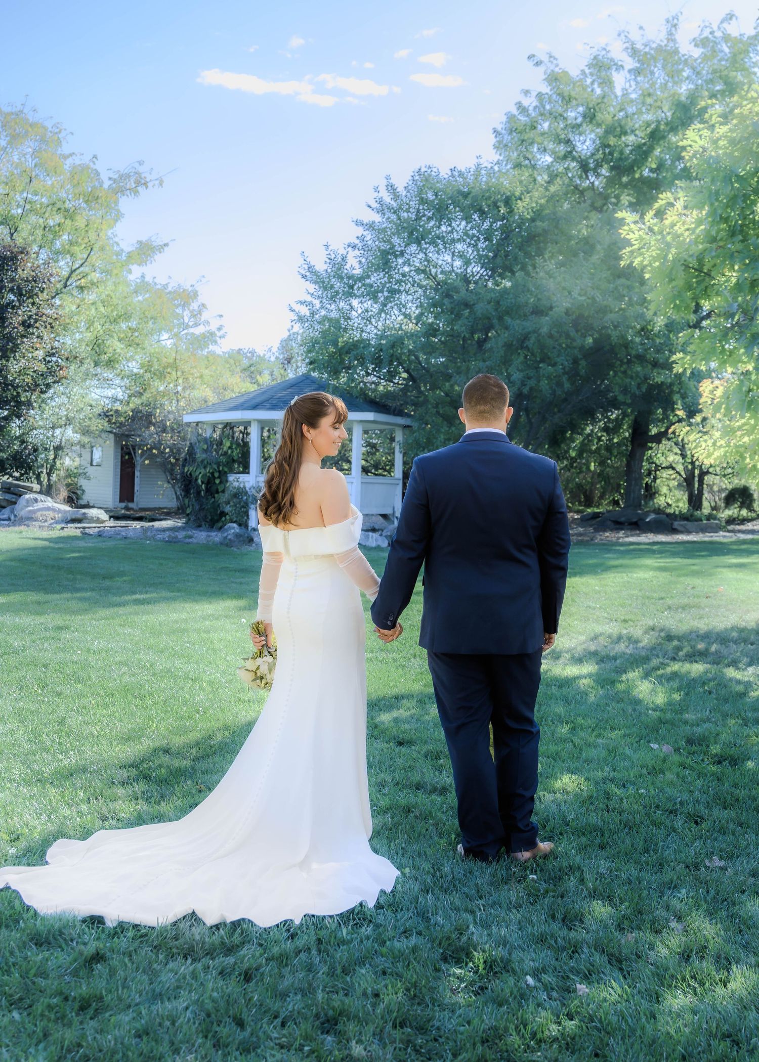 A couple walks through a lush green garden on their wedding day with trailing white dress.