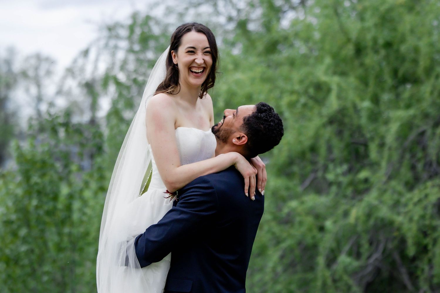 Joyful wedding couple sharing a candid moment outdoors with green foliage in the background.