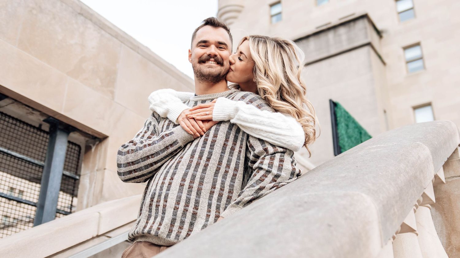 A couple shares a tender moment while dancing together on a city street with tall buildings in the background.