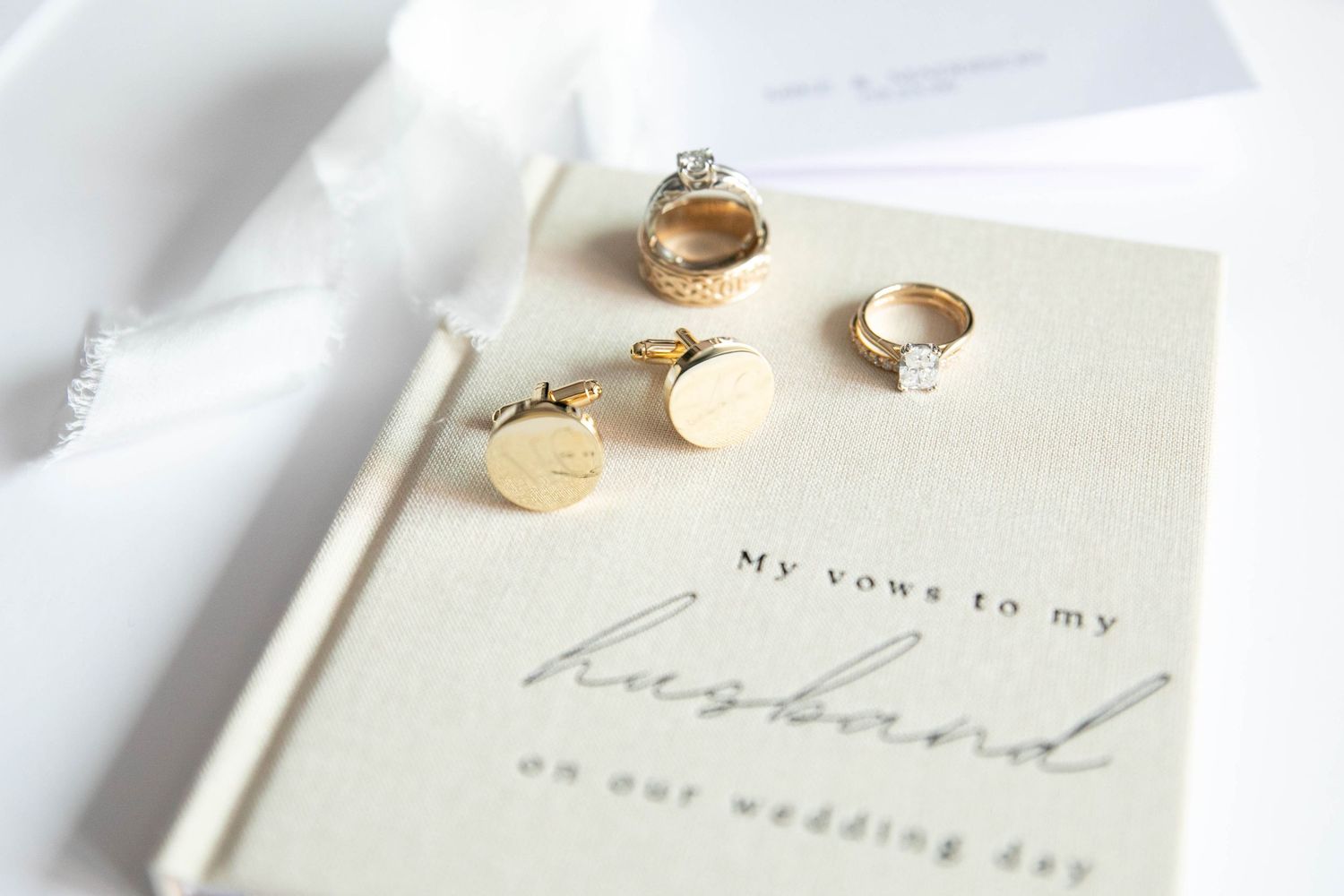 Gold wedding rings, cufflinks, and diamond engagement ring displayed on a vow book reading My Vows to My Husband.