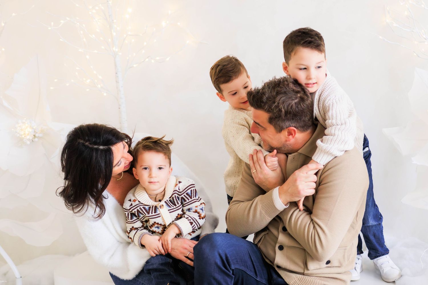 A candid family moment captured during a holiday photoshoot with white Christmas trees in the background.