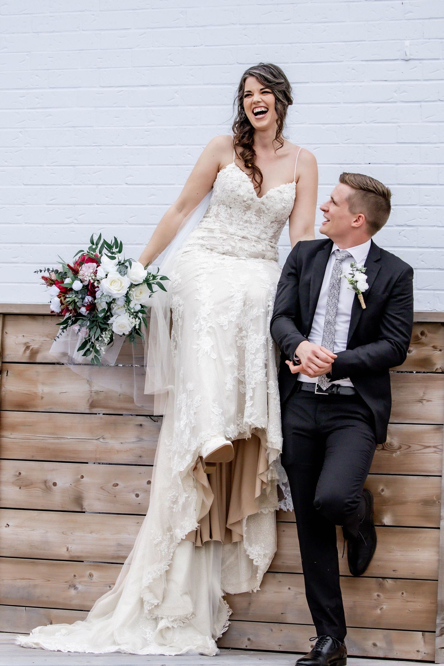 A playful wedding couple poses together against a rustic wooden wall backdrop during their photoshoot.