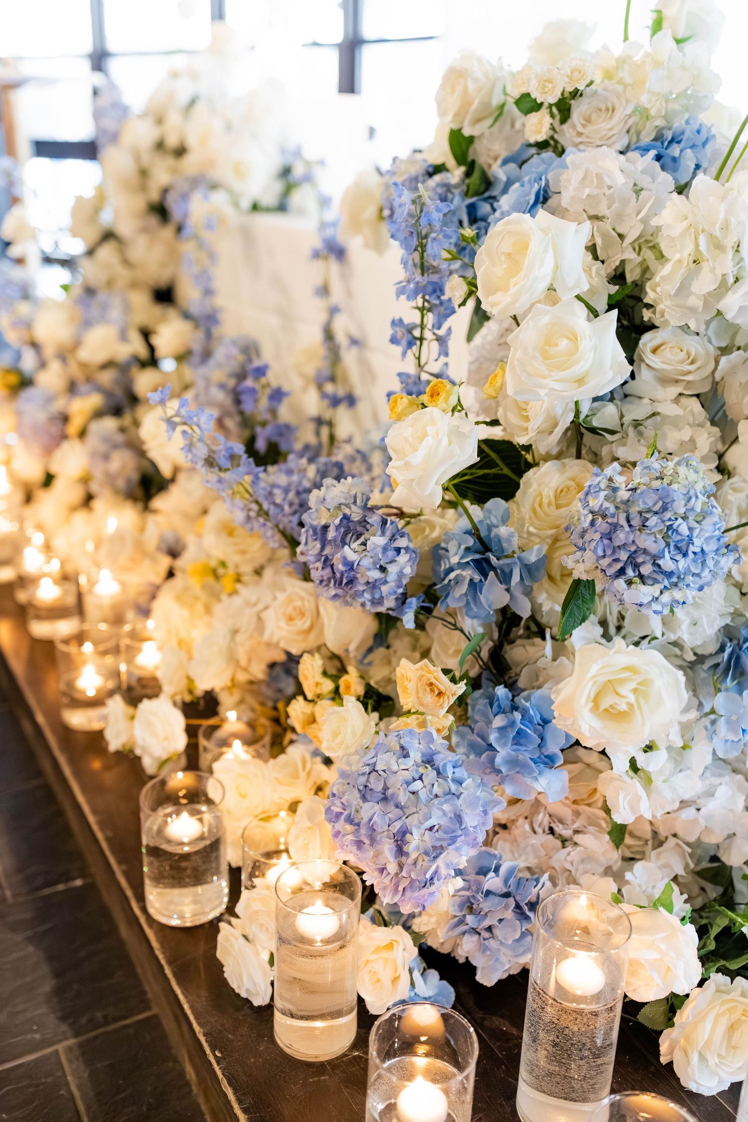 Lush wedding floral arrangement with blue hydrangeas, white roses, and glowing candles.