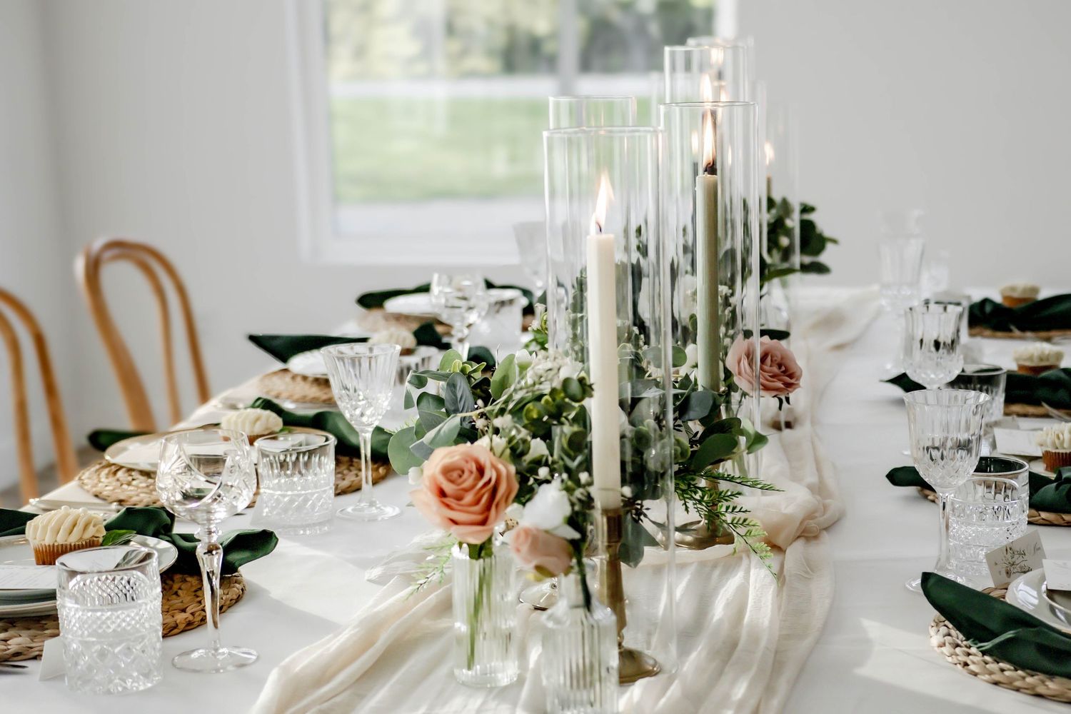 Wedding table decor with tall glass candleholders and fresh floral arrangements in soft peach tones.