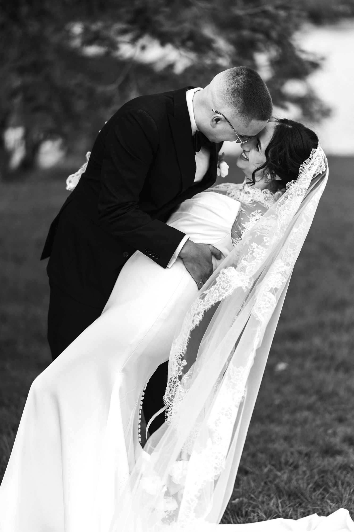 Black and white photo of groom dipping bride in a romantic kiss outdoors on their wedding day.