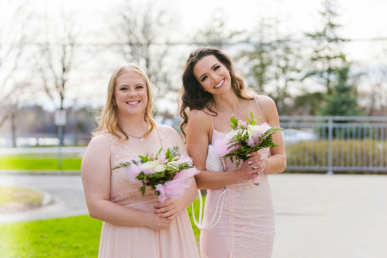 Wedding party members in pink dresses smile while holding pink and white floral bouquets.