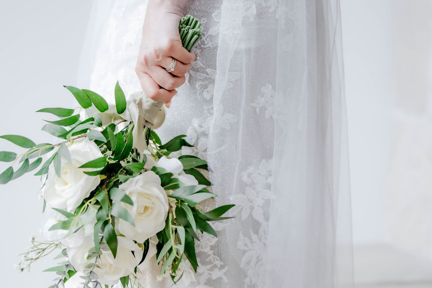 Ethereal bridal portrait showing white floral bouquet with cascading greenery against light background.