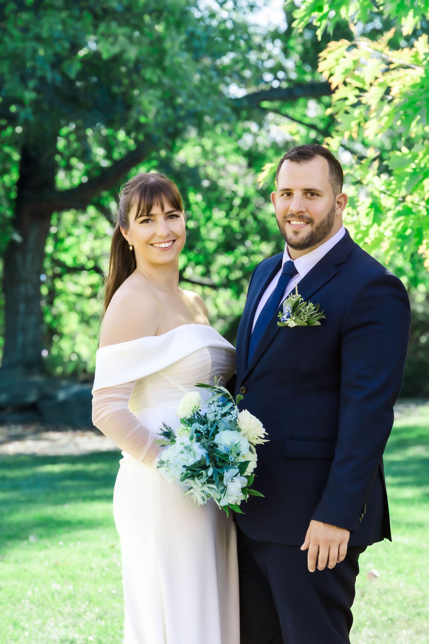 A couple shares a romantic moment outdoors in a garden setting, with the bride in white and groom in navy.