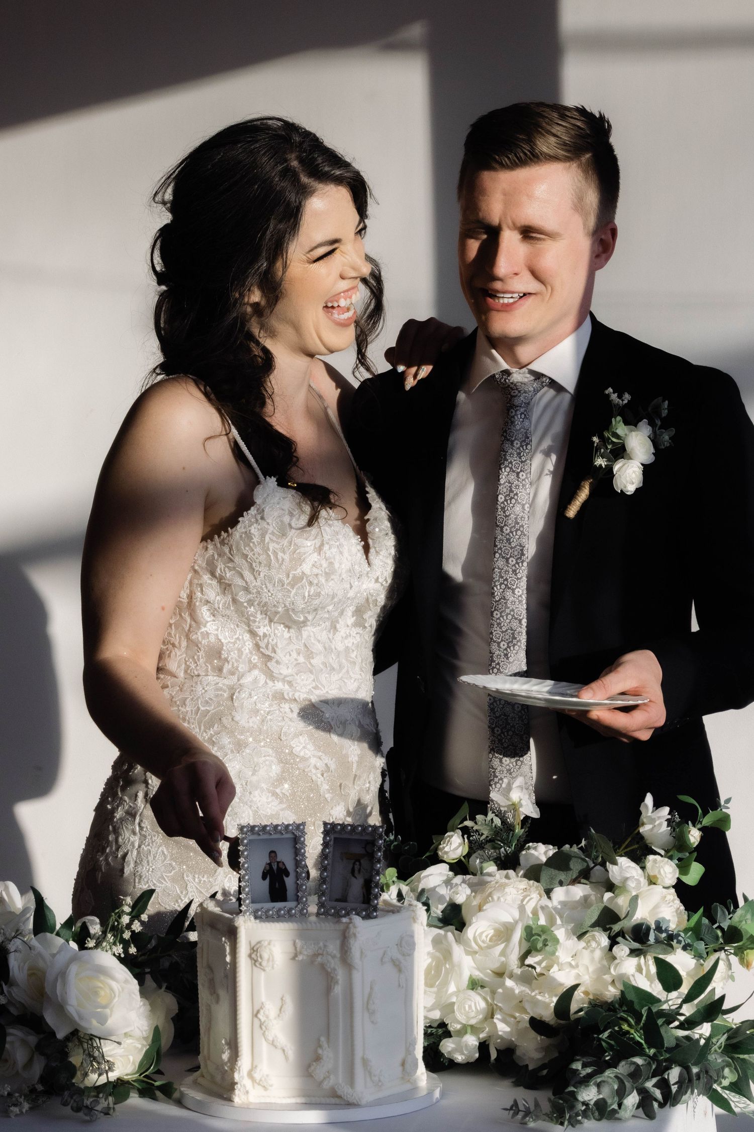 Wedding cake cutting sequence with white flowers and dramatic shadows.