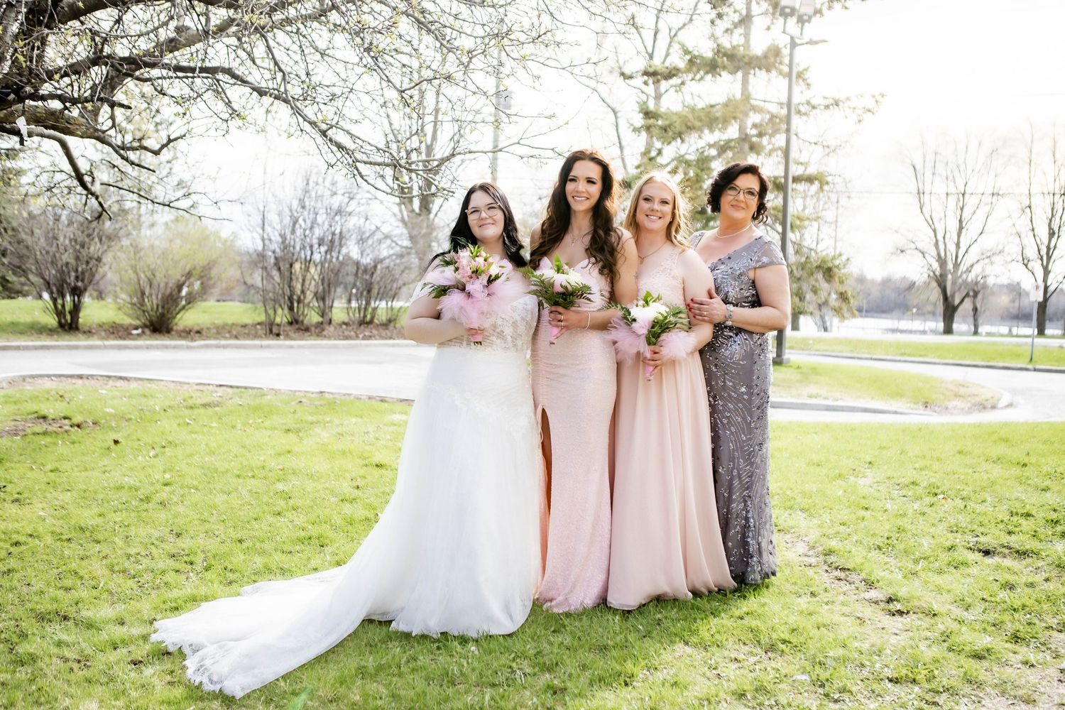 Wedding party stands on green lawn with blooming trees in background wearing pink and white dresses.