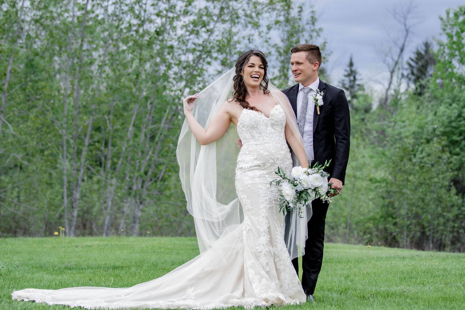A romantic wedding portrait captures a couple embracing in a serene outdoor setting with spring greenery.