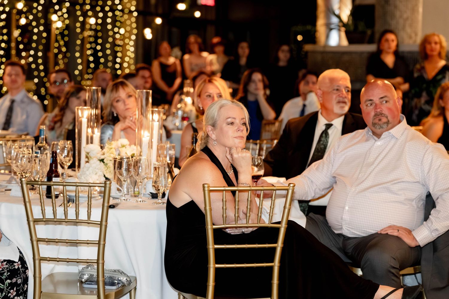 Elegantly dressed guests seated at candlelit tables during a formal gala event in a beautifully decorated venue.