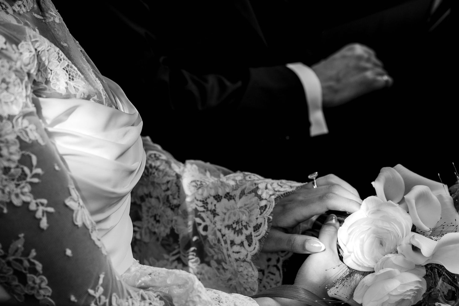 Black and white wedding photo of bride in lace gown holding white floral bouquet with groom in dark suit.
