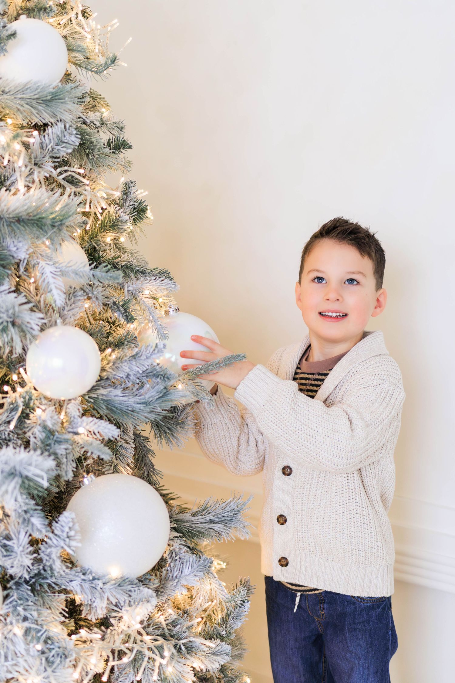 Candid moment decorating a white Christmas tree wearing cream cardigan and jeans,Ottawa family photographer.