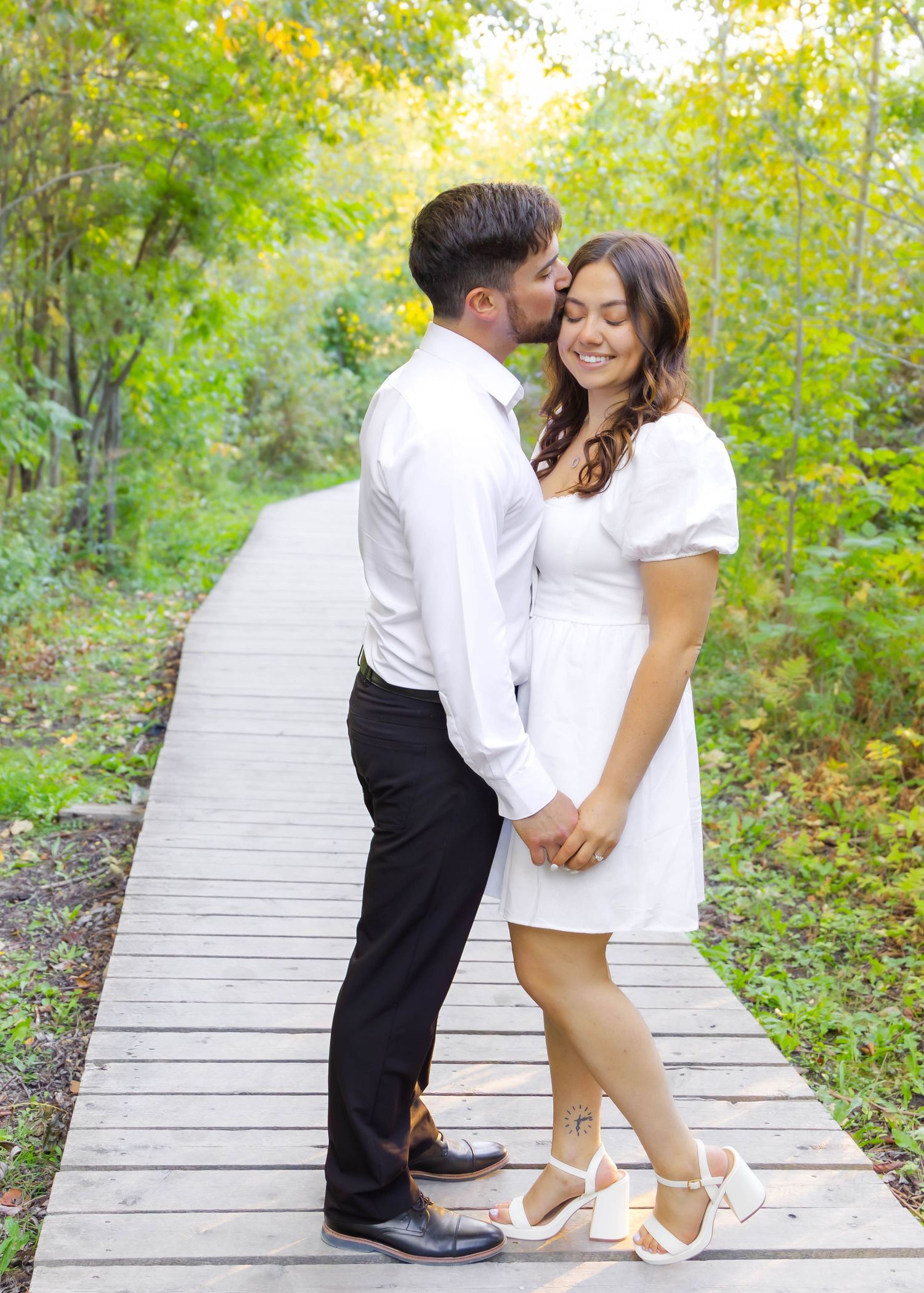 Dancing couple share playful moments on a wooden boardwalk in a natural setting.