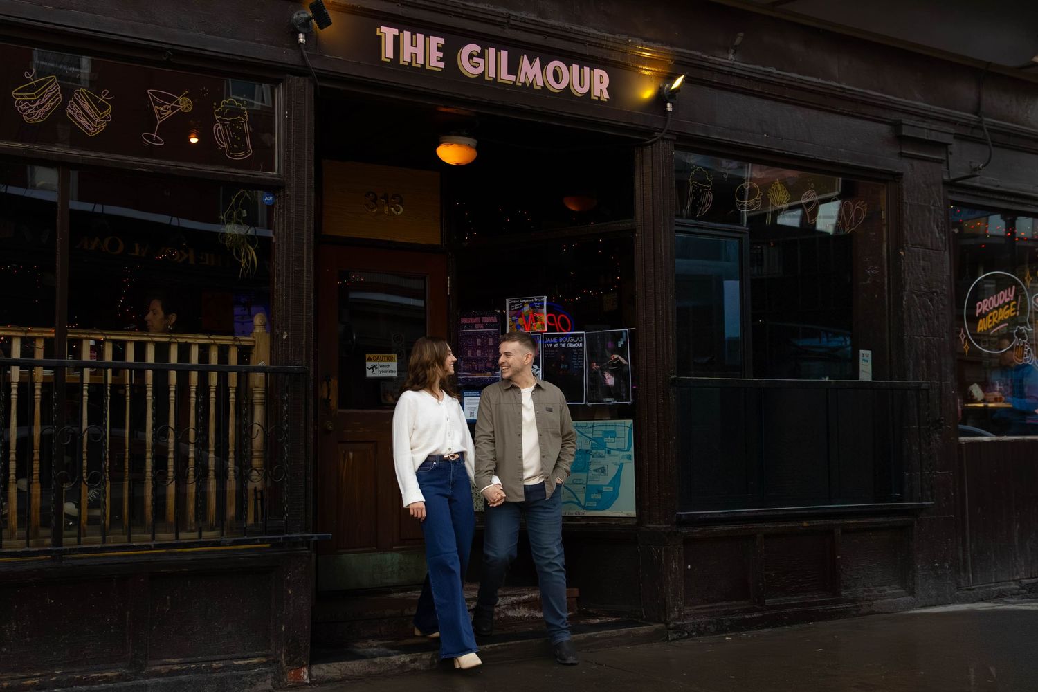 Two people stand outside The Gilmour bar entrance at night in a dark urban setting.