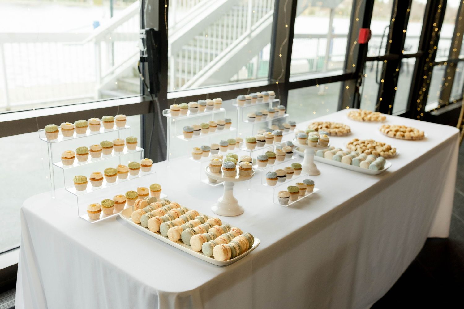 Elegant dessert table with cupcakes, macarons, and cookies displayed on tiered stands at a wedding reception.