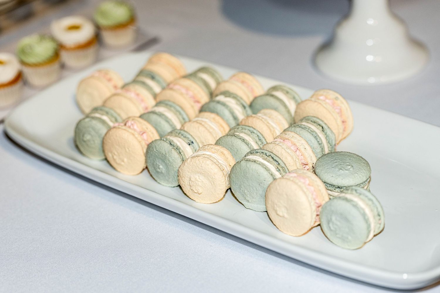 Elegant white and mint green French macarons arranged in rows on a rectangular white serving platter.
