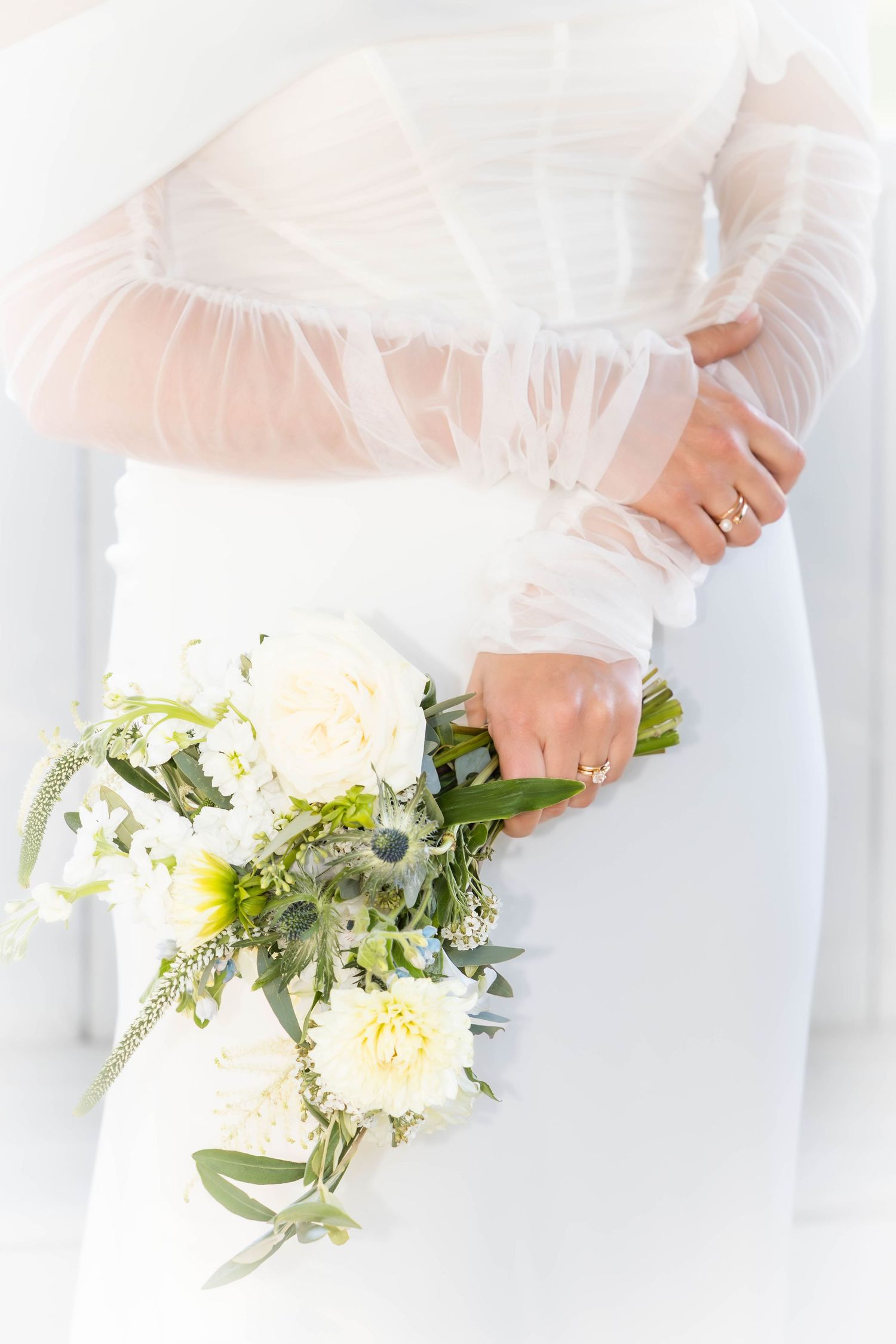 Wedding bouquet details with white flowers and greenery against a light background.