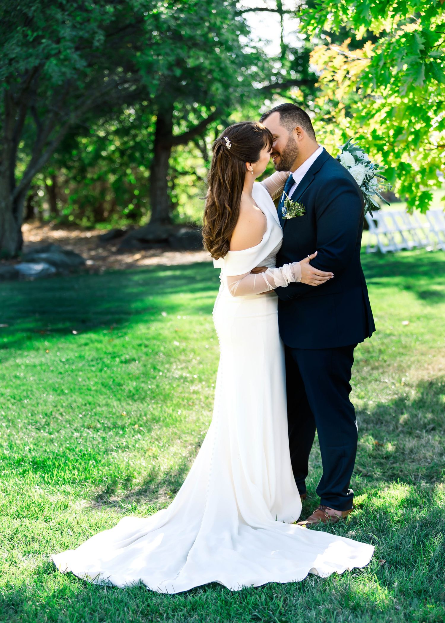 A romantic wedding couple shares intimate moments in a lush green garden setting with flowing white dress and navy suit.
