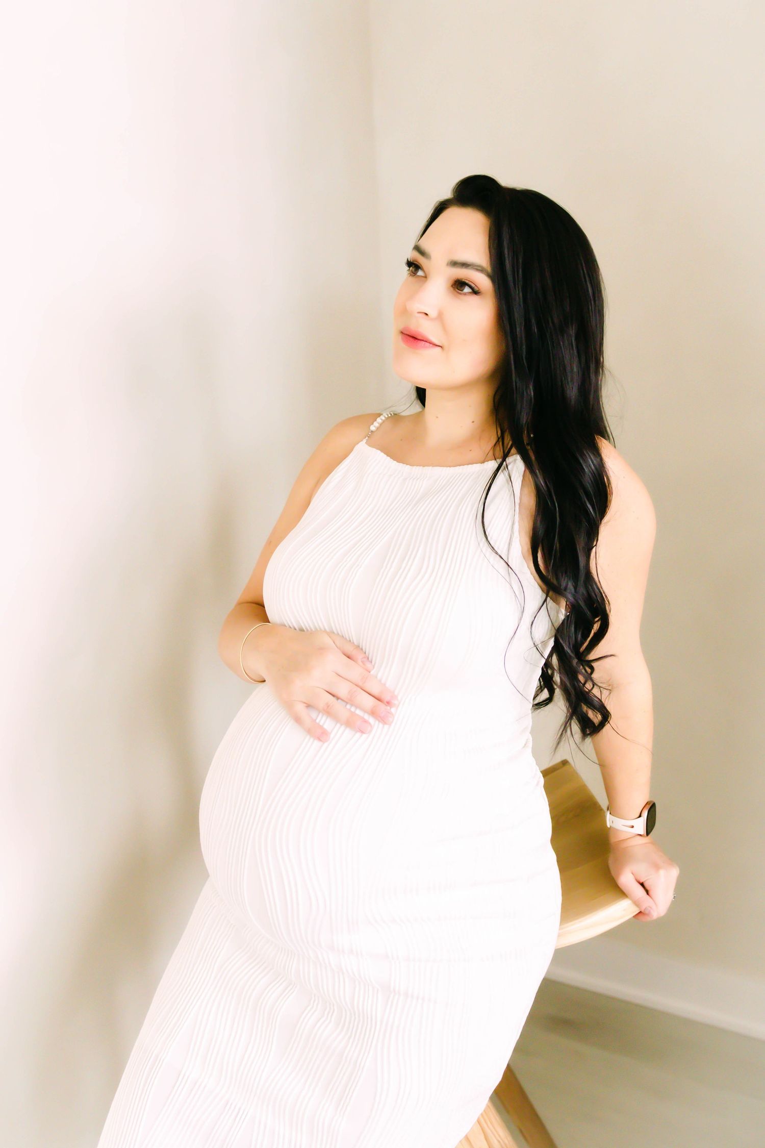 Woman in white sleeveless dress poses gracefully against neutral wall in artistic portrait series.